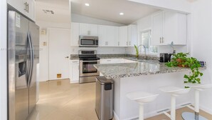 Una cocina moderna con armarios blancos, electrodomésticos de acero inoxidable, una encimera de granito y una pequeña isla con taburetes de bar.