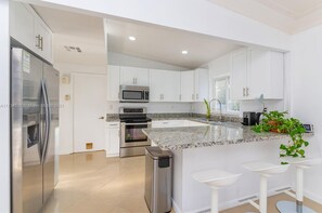 A modern kitchen with white cabinets, stainless steel appliances, a granite countertop, and a small island with bar stools. - Amazing backyard for Family vacation with heated pool.  (Wilton Manors)