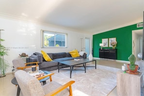 A modern living room with a grey sofa, yellow pillows, a coffee table, and a green accent wall.