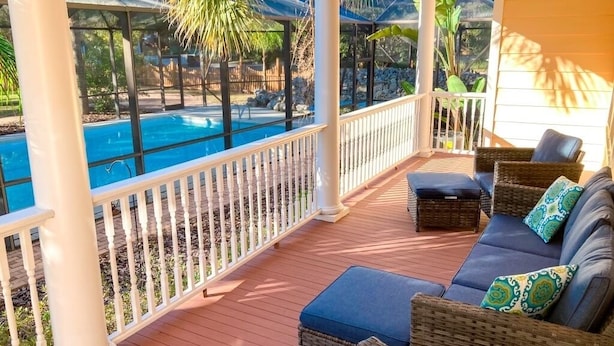 A covered outdoor area with a pool, wicker furniture, and a white railing. - University House - 8 Bedrooms - Walk to UF / Stadium (Gainesville)