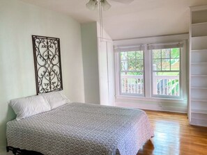 Ein Schlafzimmer mit einem Bett, einem Fenster mit Blick auf Grünflächen und einem Deckenventilator.