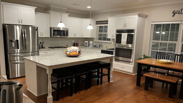 A modern kitchen with white cabinetry, stainless steel appliances, a large island with bar stools, and pendant lighting.