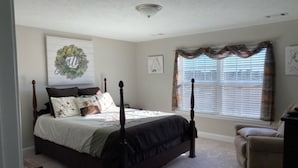 A bedroom with a four-poster bed, a window with blinds, and a wall-mounted artwork.
