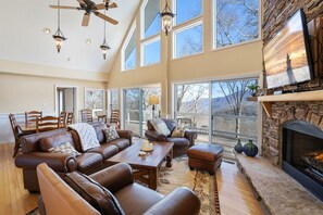 A spacious living room with a fireplace, leather furniture, and large windows offering a view of the outdoors. - Delightful Home Atop Sugar Mountain (Sugar Mountain)