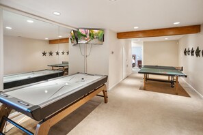 Una mesa de billar con una pared espejada y una mesa de ping pong en una sala con una viga de techo de madera y un televisor montado en la pared.