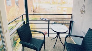 A balcony with two wicker chairs and a small round table, overlooking a parking area and buildings. - Specious roofapartment apartment, tropical velvet (Helsinki)