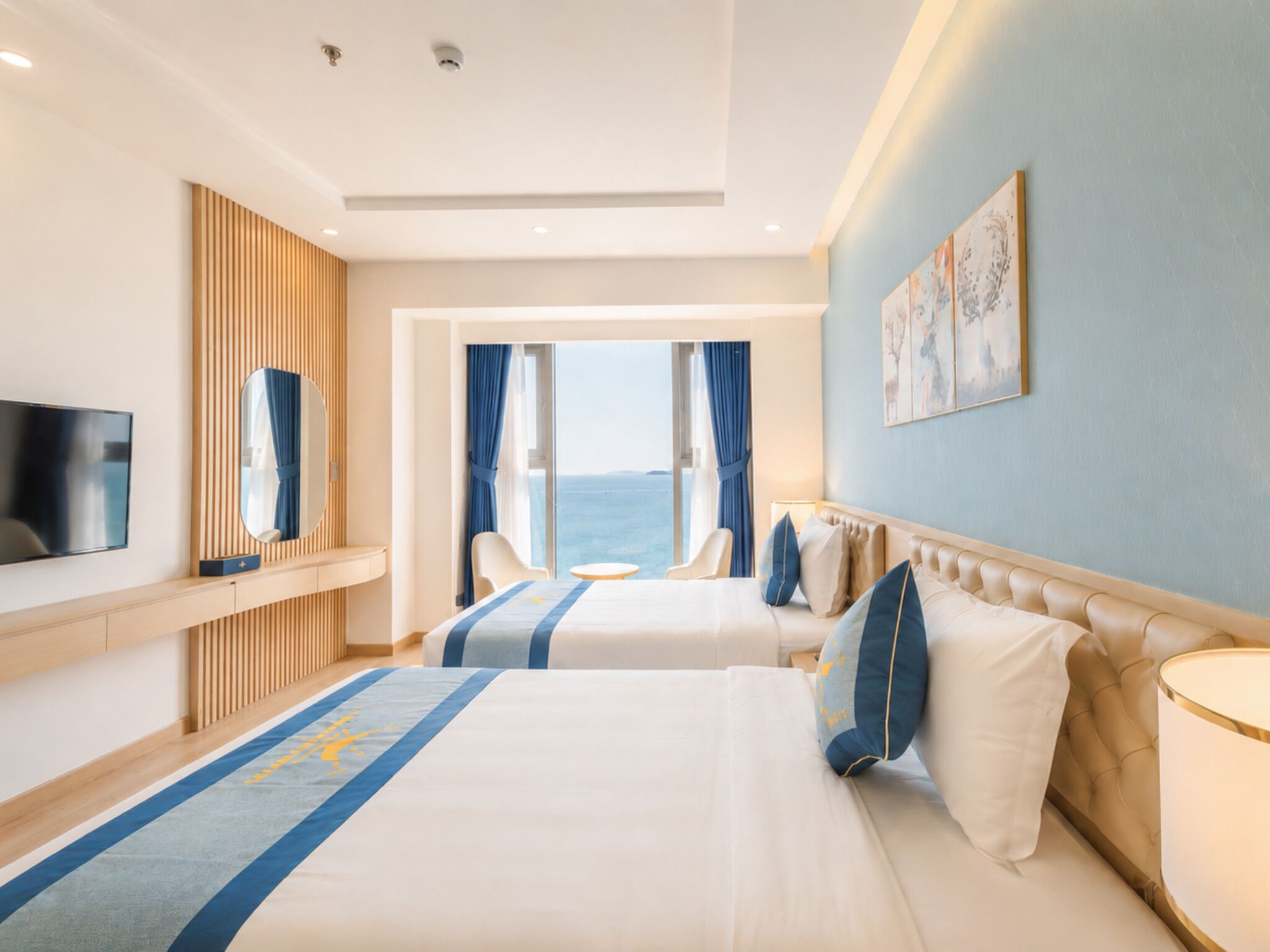 A hotel room with two beds, a TV, a large window with a view, and a painting on the wall.