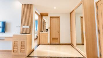 A modern hotel room with a wooden wardrobe, a desk with a flat-screen TV, and a large mirror.