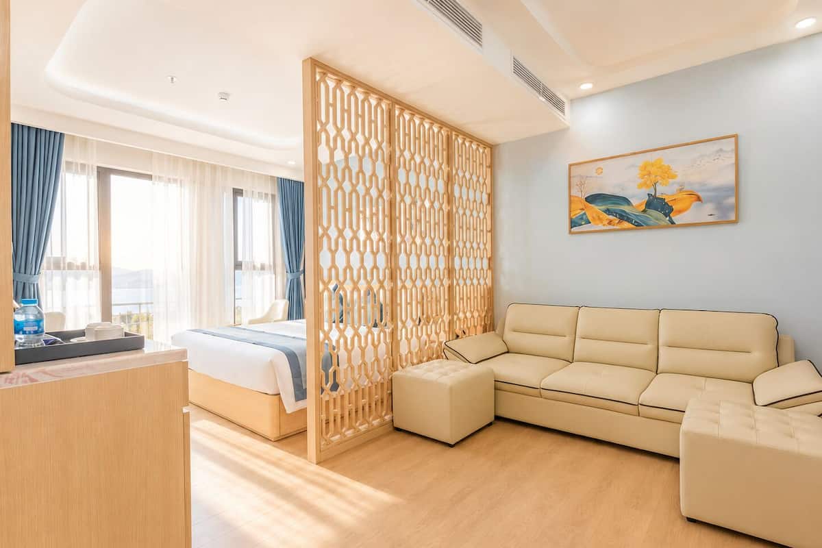 Habitación de hotel con cama, sofá, un separador decorativo, un cuadro y vistas al exterior.