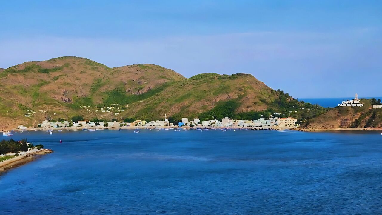 Eine Küstenstadt mit einem Yachthafen, Gebäuden und Hügeln im Hintergrund.