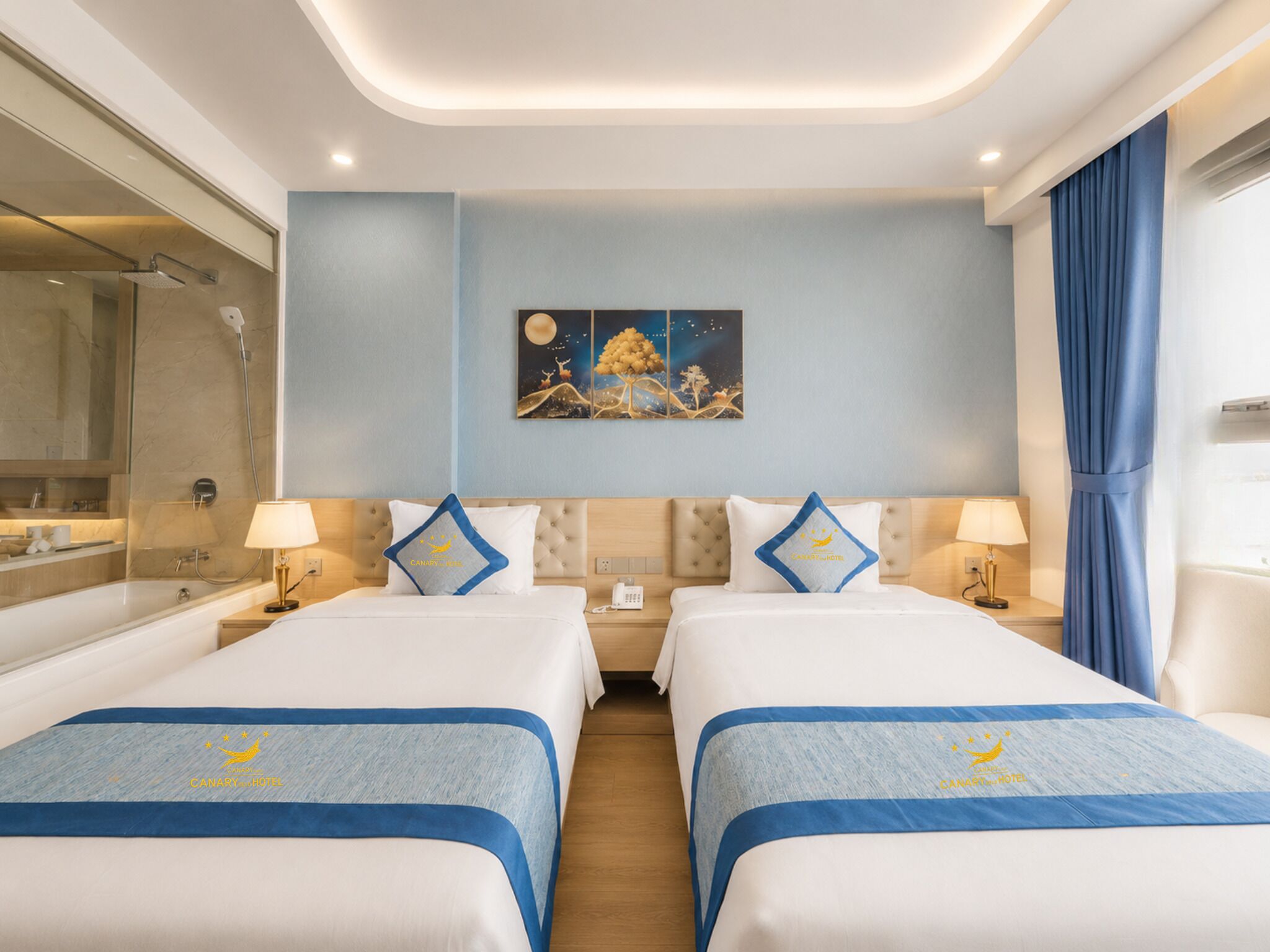 Ein Hotelzimmer mit zwei Betten, einem Nachttisch, einem Gemälde, einem Badezimmer und einem Vorhang.