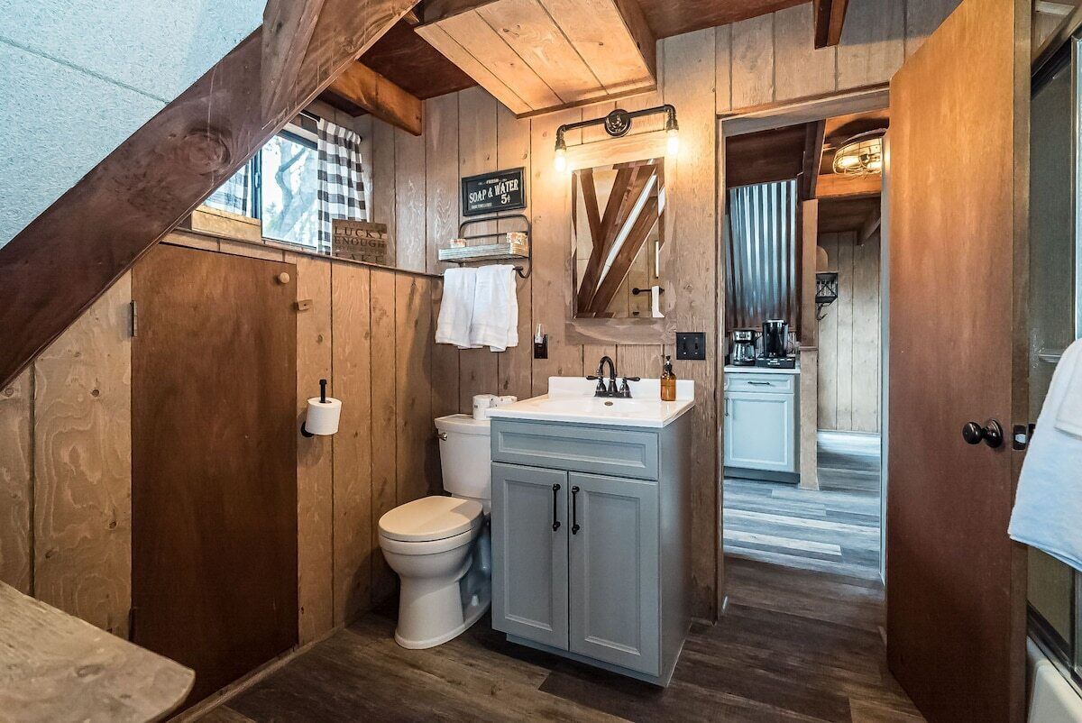 Une salle de bain rustique avec des murs en bois, des toilettes blanches, un lavabo avec un miroir et une serviette accrochée au mur.