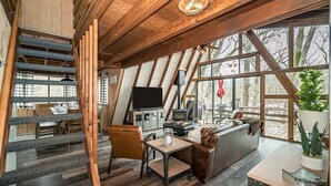 Ein gemütlicher Loft-Raum mit Holzboden, einem großen Fenster, einem Fernseher, einer Couch und einer Treppe.