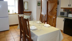 Un comedor con una mesa lista para dos personas, sillas de madera, un refrigerador blanco, un microondas y un mueble con salpicadero de azulejos.