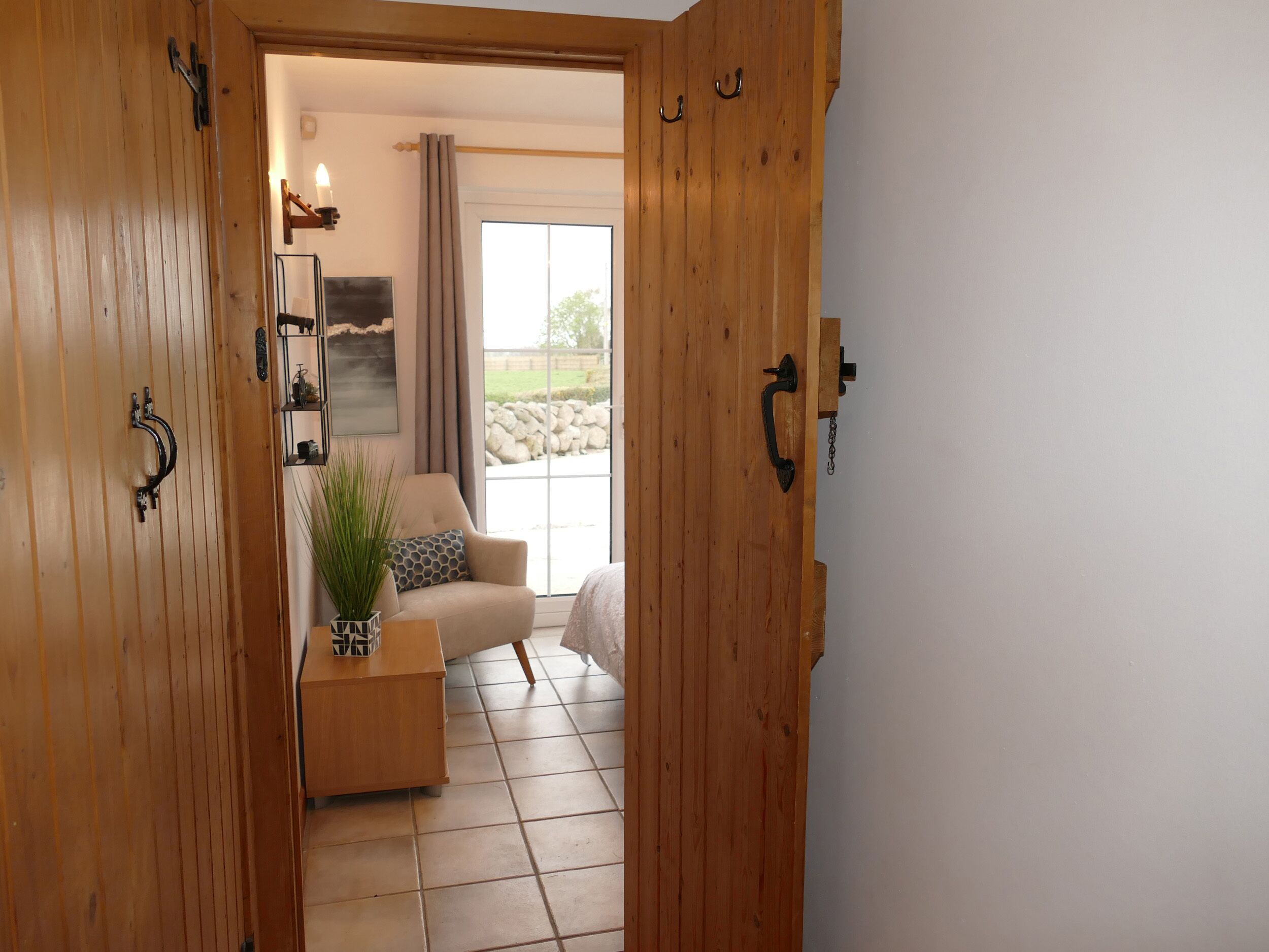 Una puerta de madera que da a una sala de estar con un sofá color crema, una mesita con una planta y una ventana con cortinas.
