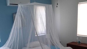 A room with two beds covered by mosquito nets, a ceiling fan, an air conditioning unit, and a window with blinds. - Villa Olivia Poolside, Dive villa, 300 m from the Ocean! (Kralendijk)