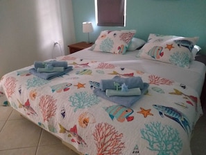 A bed with a colorful sea-themed bedspread, two pillows, and folded towels on a headboard.