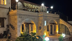 A stone building with arched doorways, a balcony with hanging lights, and a staircase leading to an upper level.