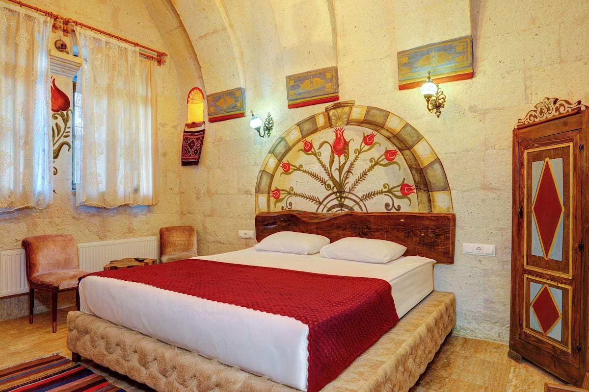 A bedroom with a large bed, a wooden headboard, a red blanket, a chair, and a wardrobe.