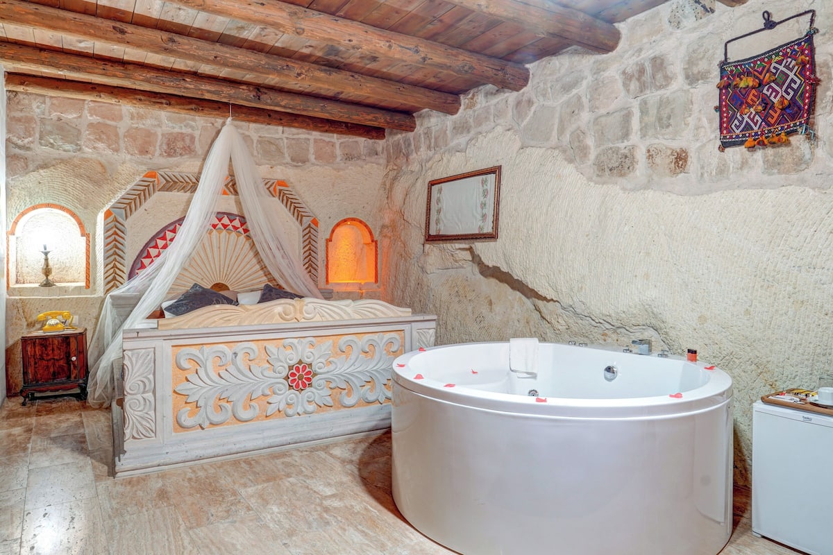 A bedroom with a large bathtub, a bed with ornate headboard, and a stone wall.