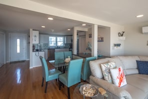 Un vaste espace de vie comprenant un canapé, des fauteuils turquoise et une table à manger en verre.