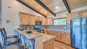 A kitchen with wooden cabinets, granite countertops, a stainless steel refrigerator, and a stone backsplash. - Spacious, Near Midtown w/ Grill+Deck+Views+Arcade (Ruidoso)
