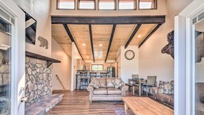 A spacious living area with a stone fireplace, wooden floors, a large sofa, and a dining table. - Spacious, Near Midtown w/ Grill+Deck+Views+Arcade (Ruidoso)