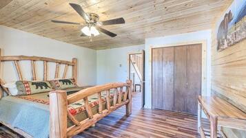 A wooden-floored bedroom with a bed, a wooden headboard, a ceiling fan, and a door.
