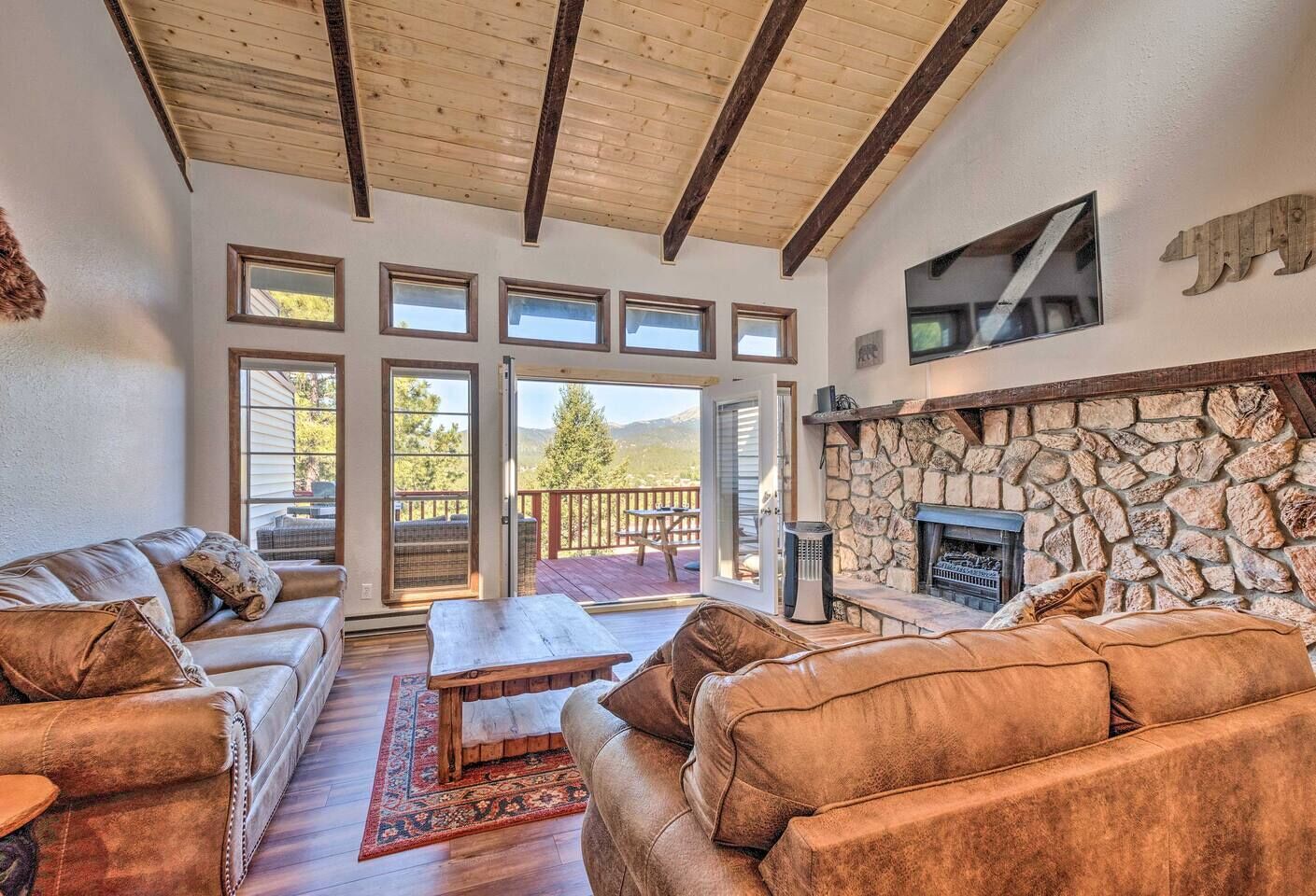 A spacious living room with leather sofas, a stone fireplace, large windows, and a deck area.