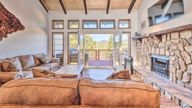 A spacious living room with a leather sofa, a stone fireplace, and a view of the outdoors. - Spacious, Near Midtown w/ Grill+Deck+Views+Arcade (Ruidoso)