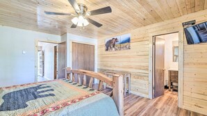 A wooden cabin interior with a bed, a ceiling fan, a wooden staircase, and a bear picture on the wall. - Spacious, Near Midtown w/ Grill+Deck+Views+Arcade (Ruidoso)