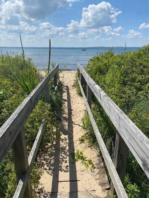 Un sendero de madera que conduce a una playa con vista despejada al mar y montañas distantes.