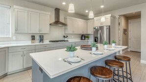 A modern kitchen with white cabinets, a central island with stools, stainless steel appliances, and pendant lighting. - Paradise Village Resort 103: Resort View, Private Hot Tub, Short Walking distance to Resort (Santa Clara)