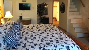 Ein Schlafzimmer mit Bett, Fernseher, Lampe, Pflanze und einer Treppe.