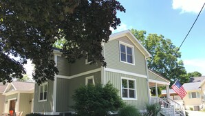 Ein zweistöckiges Haus mit Veranda, kleinem Vorgarten und amerikanischer Flagge.