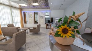 Eine moderne Hotelhalle mit einer großen Sonnenblumen-Dekoration, bequemen Sitzgelegenheiten und einem Fernseher im Hintergrund.