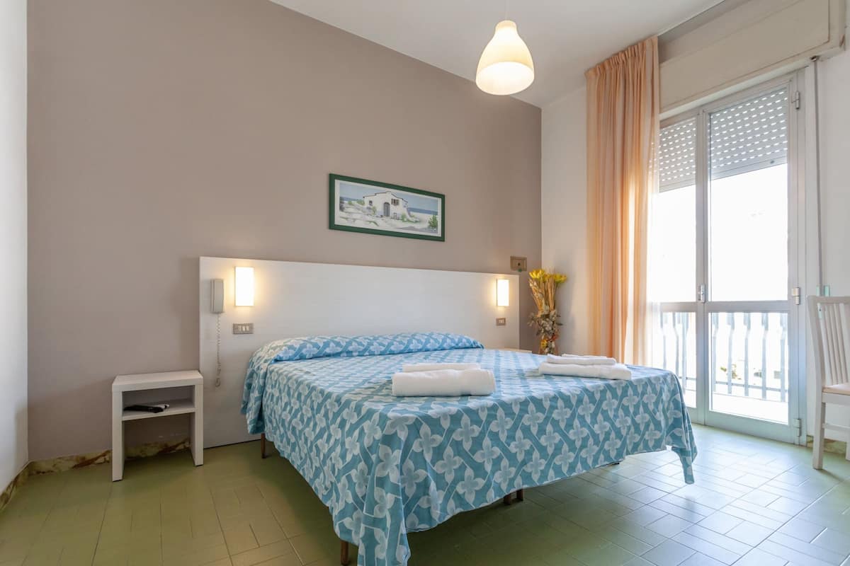 Ein Schlafzimmer mit Bett, Nachttischen, einem Bild und einem Fenster mit Vorhängen.