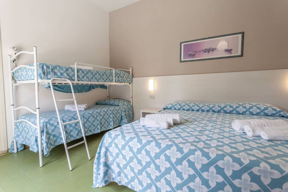 Ein Zimmer mit Etagenbetten, einem Bett mit gemustertem Bettbezug, einer Wandleuchte und einem gerahmten Bild.