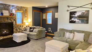 Un salon chaleureux avec un mur en pierre, une cheminée, deux canapés et un grand tableau représentant un lac.