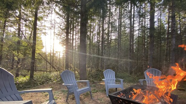 Une zone boisée avec des fauteuils Adirondack et un foyer en métal où brûle un feu.