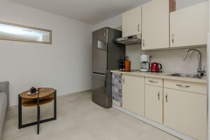 Compact kitchen with a stainless steel refrigerator, coffee maker, and sink, plus a small table and chair.