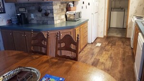Una cocina con armarios de madera, microondas, refrigerador y una mesa de comedor con sillas.