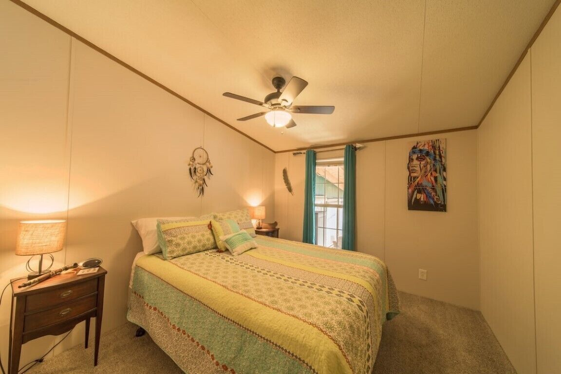 A bedroom with a bed, a nightstand, a ceiling fan, a wall-mounted dreamcatcher, and a window with curtains.