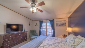 Un dormitorio con cama, cómoda, televisor, silla, ventana con cortinas y ventilador de techo.