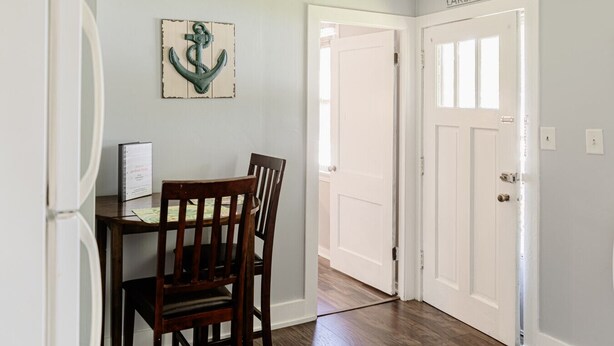 A dining area with a wooden table and chairs, a white door labeled "LAKEHOUSE," and a wall-mounted anchor decoration.