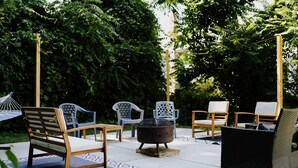 An outdoor patio area with wooden and wicker chairs, a small round table, and a fire pit.