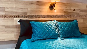 A bed with a teal quilted bedspread and two pillows, a wall-mounted lamp, and a wooden headboard with a mosaic tile accent. - Hotel Santa Cruz Residencial (San Luis Rio Colorado)