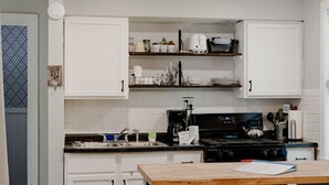 Une cuisine de taille réduite avec des meubles blancs, une cuisinière noire et une table en bois accompagnée d’un banc.