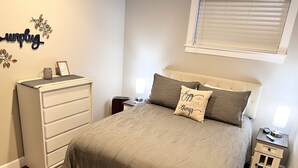 A neatly arranged bedroom with a bed, a dresser, a nightstand, and a wall decoration.
