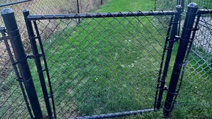 A fenced area with a grassy field and trees in the background.